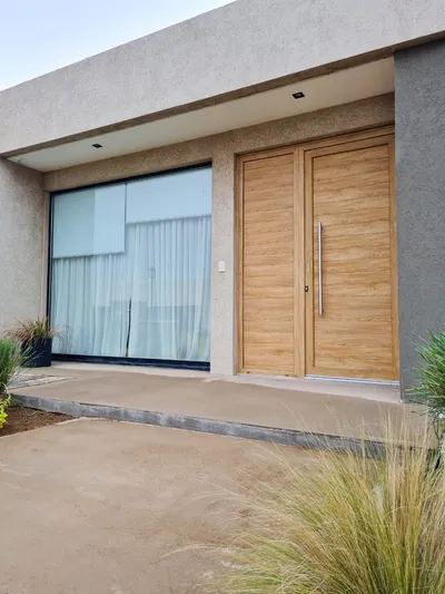 Puerta de entrada color turner y ventanal corredizo de aluminio negro bajo el alero de la casa