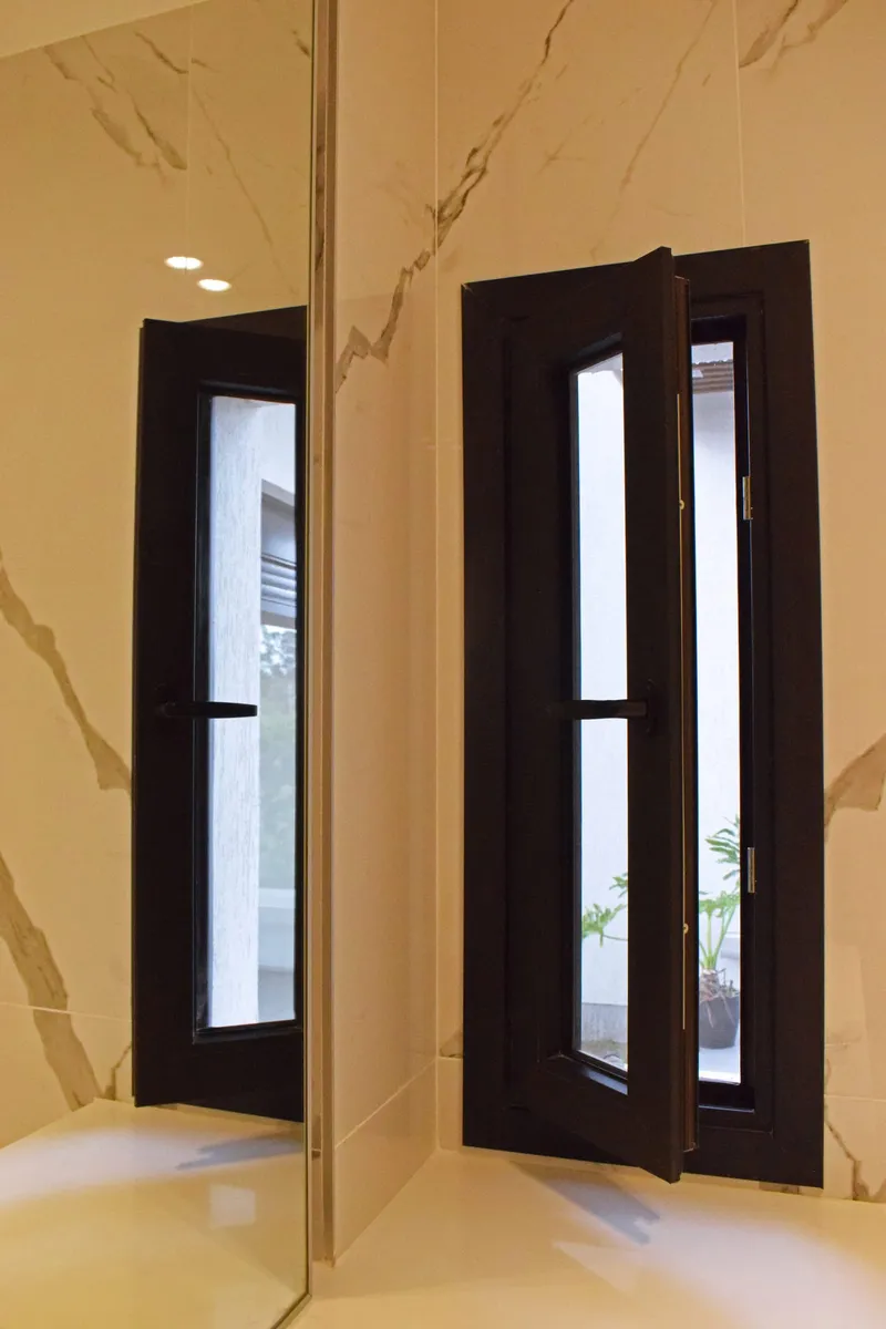 Puerta de PVC negro mate con paño vidriado vertical, reflejada en el revestimiento de mármol